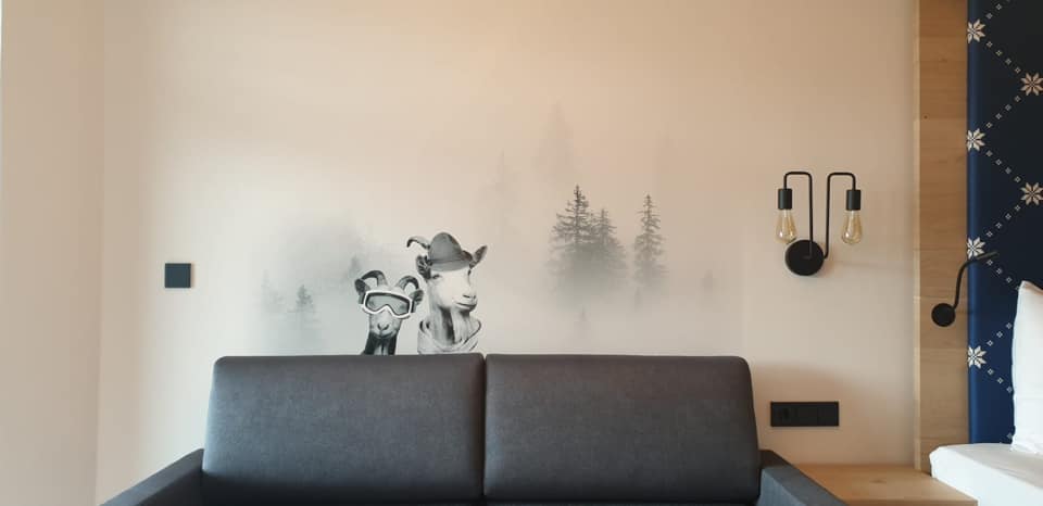 Hotelzimmer mit zwei verschmitzten Bergziegen im Nebelwald als Wandbild über dem Sofa